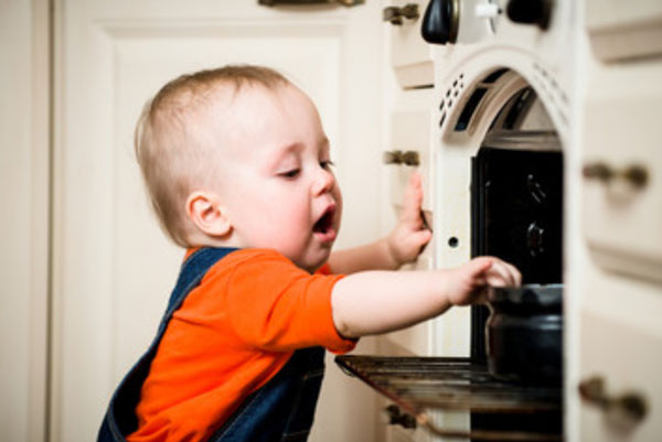 Ребенок дотрагивается до казанка , который стоит в духовке